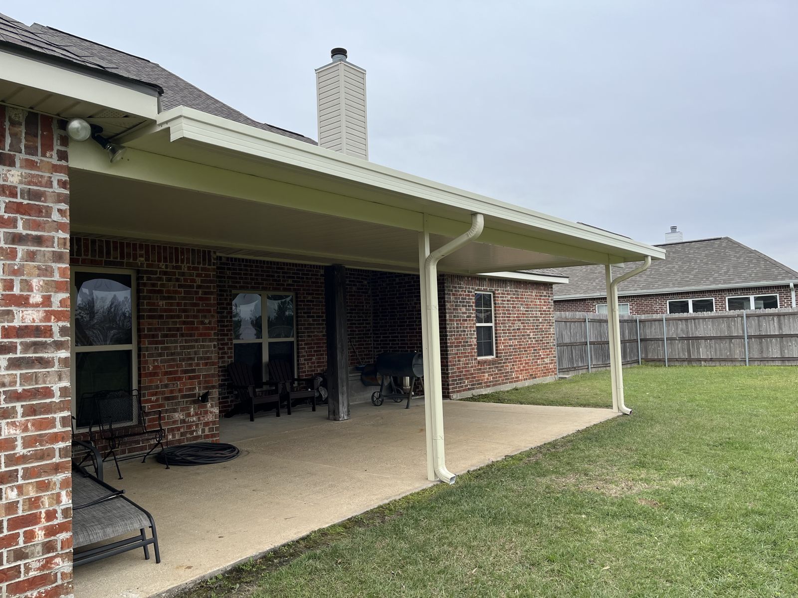 White aluminum patio cover with gutter and downspout on a brick home