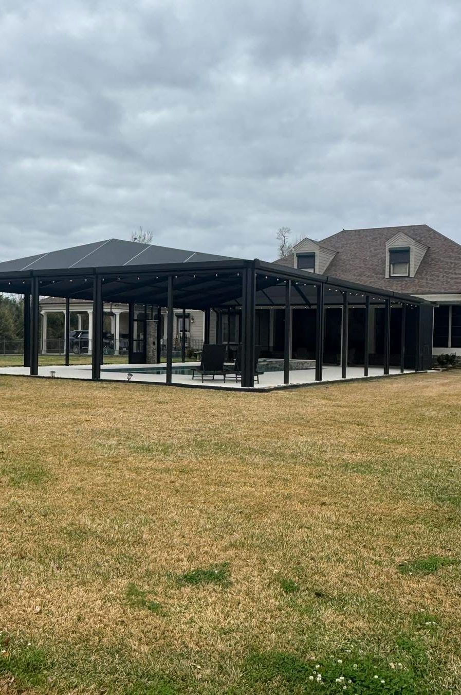 Large black-framed pavilion cover over a pool on an open lawn
