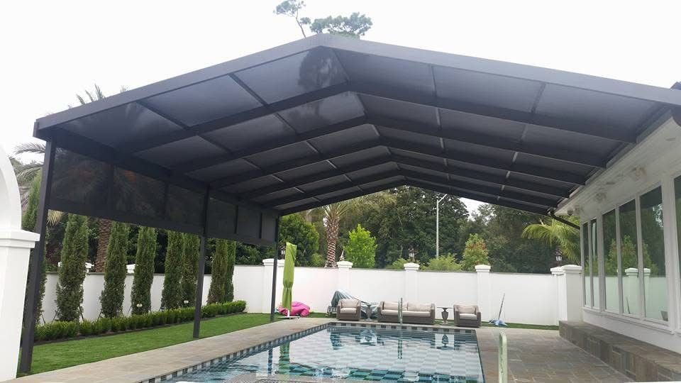Dark gabled patio cover with shade panels beside a pool