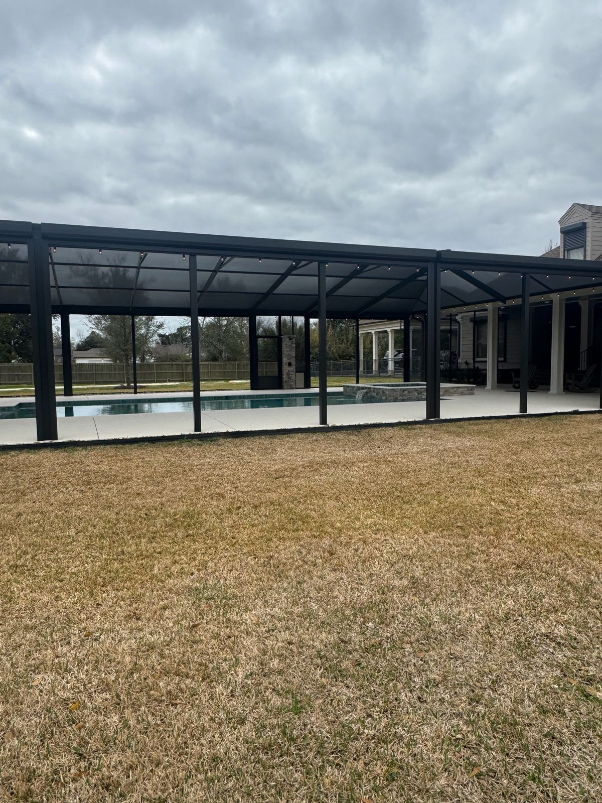 Long black-framed pavilion over a pool and spa on an open lawn