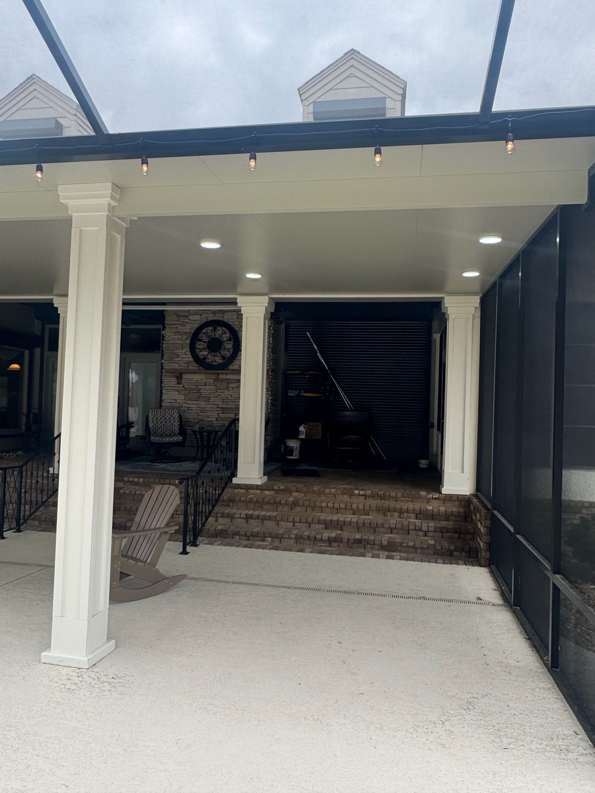 White-columned covered patio beside a dark screen wall and brick steps