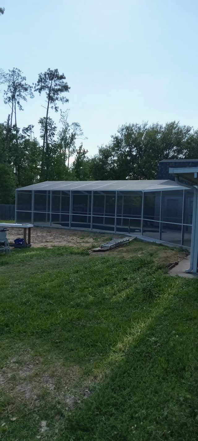 Long white-framed pool screen enclosure behind a home