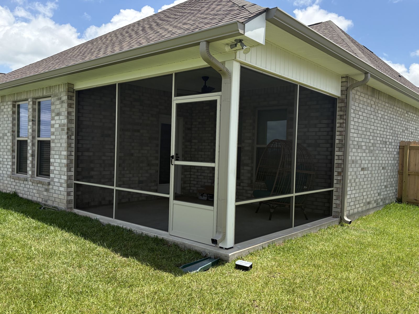 Beige fixed-screen room with screen door on a brick home