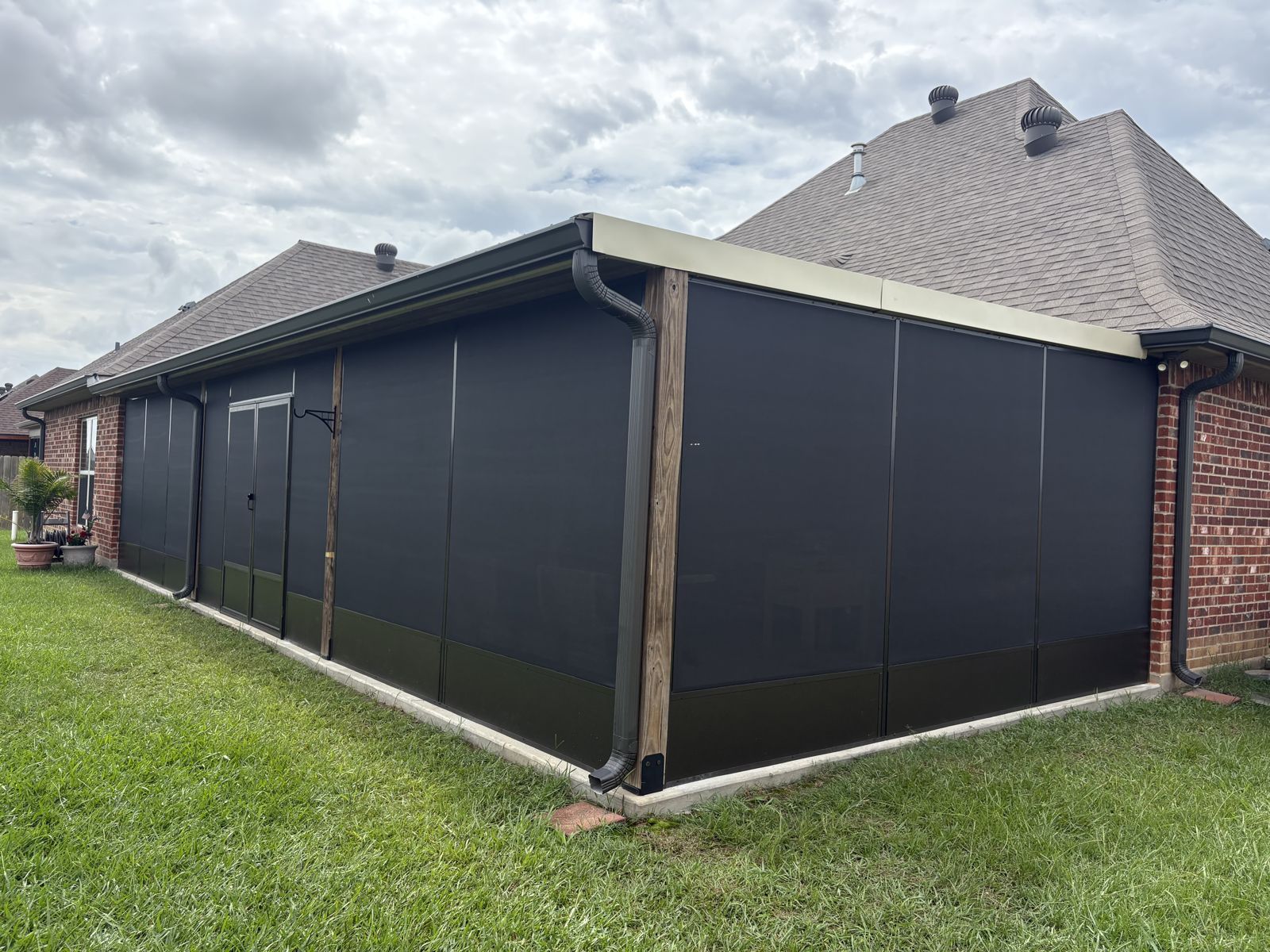Corner of a dark bronze screen room on a brick home