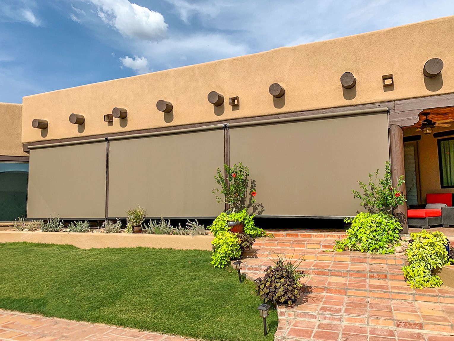 Tan motorized roller shades lowered along a stucco home's covered patio