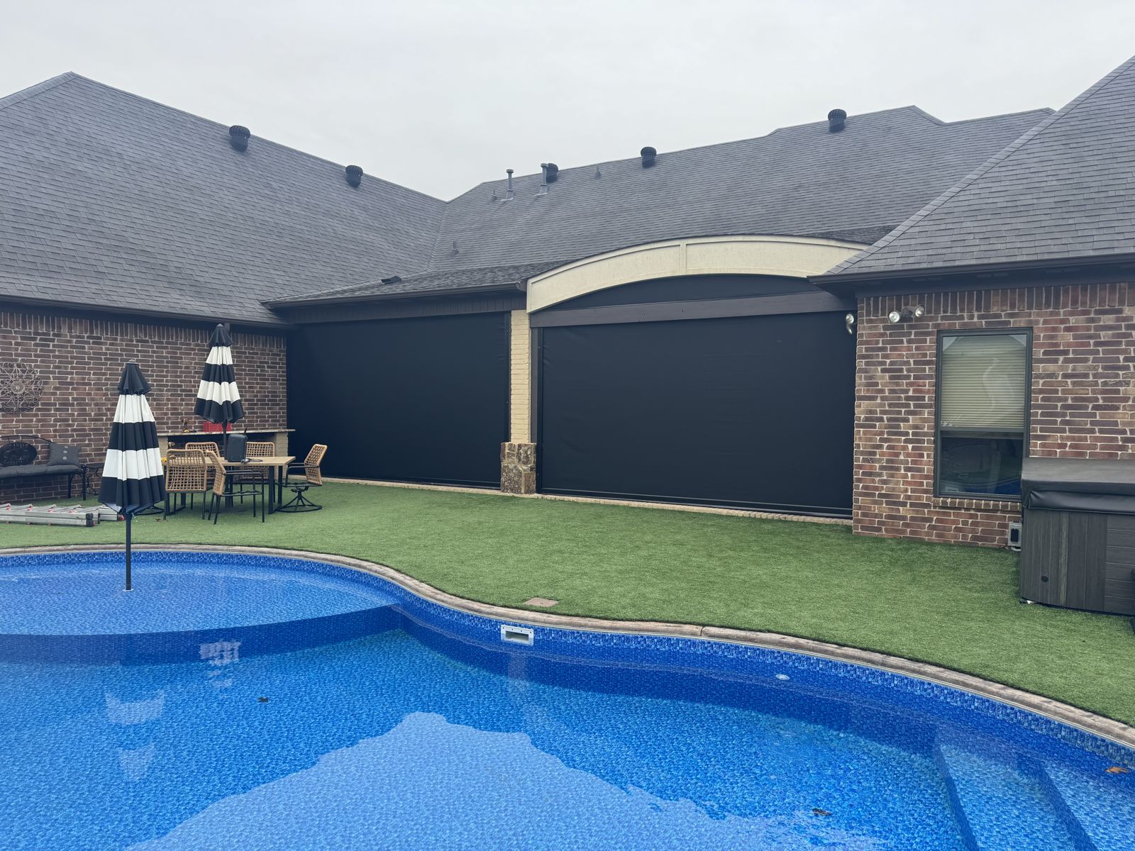 Black patio shades on a brick home seen across the back-yard pool