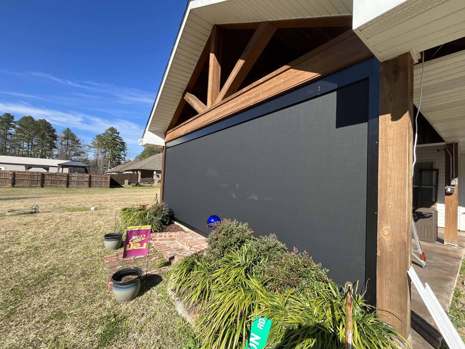 Black roller shade lowered on a timber-beam covered porch