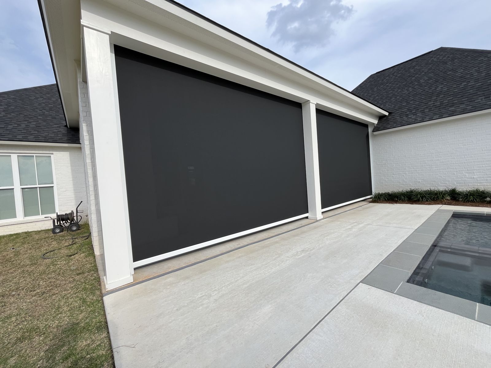 Black motorized shades on a white-columned porch beside a pool deck