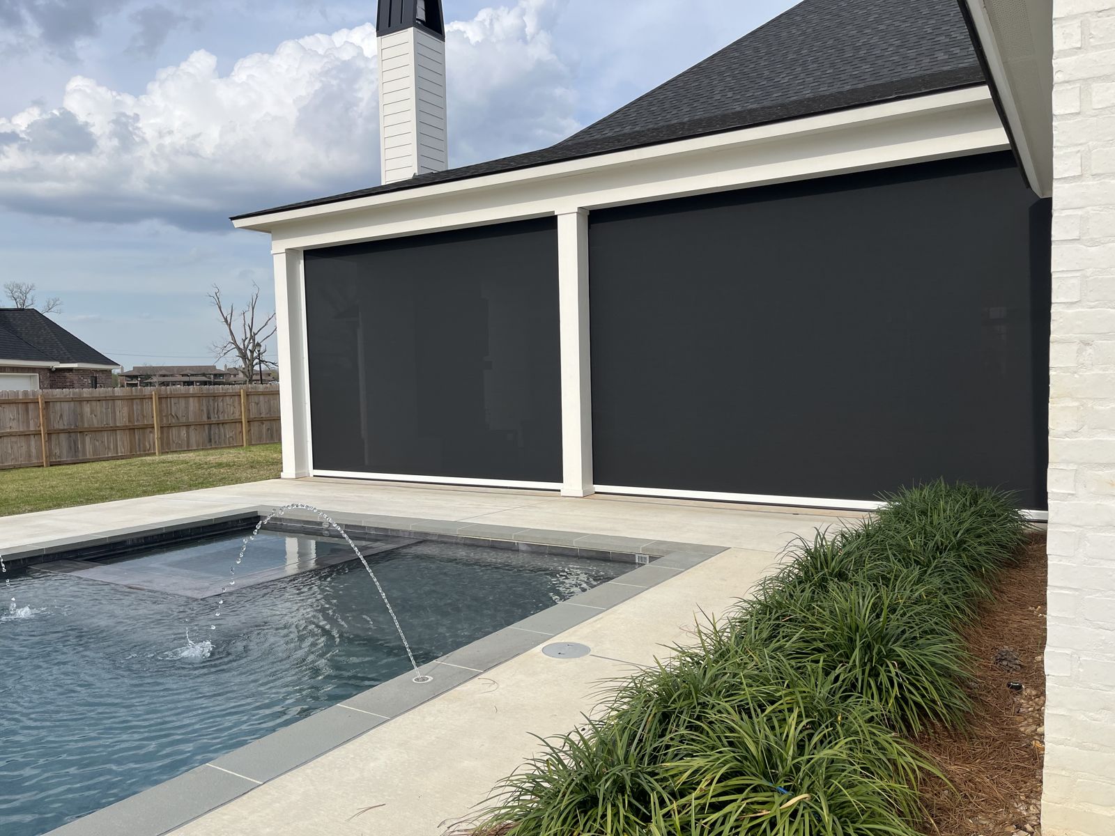 Black motorized shades lowered on a covered patio beside an in-ground pool