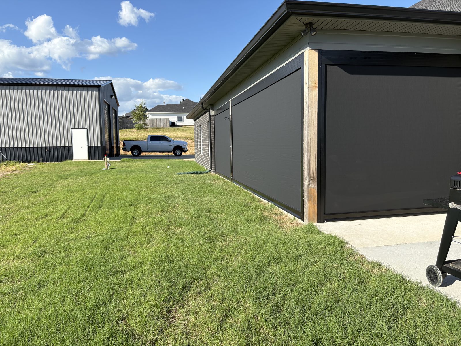 Dark motorized shades on a long covered patio next to a metal shop building
