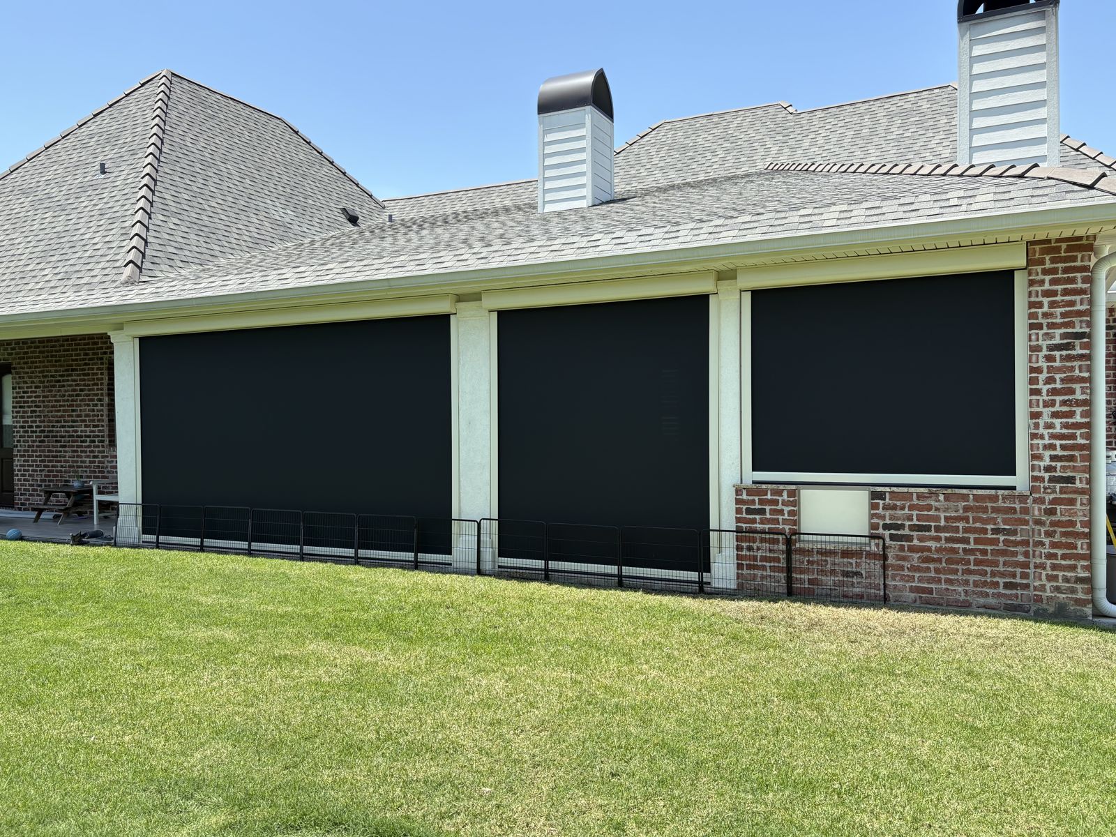 Black motorized shades lowered along a brick home back porch