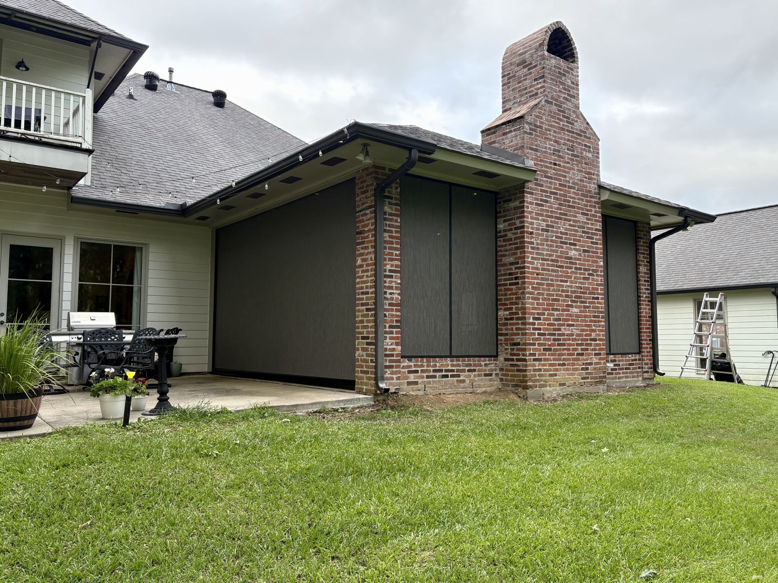 Dark roller shades on a covered patio beside a brick chimney
