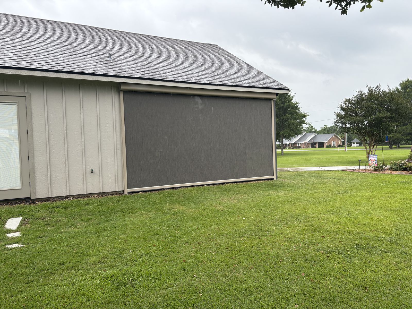 Dark roller shade lowered on a siding wall of a covered patio