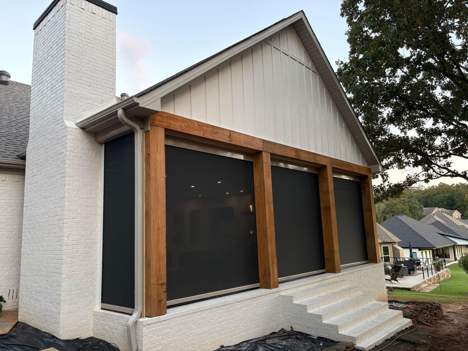 Black motorized shades between wood posts on a white brick home