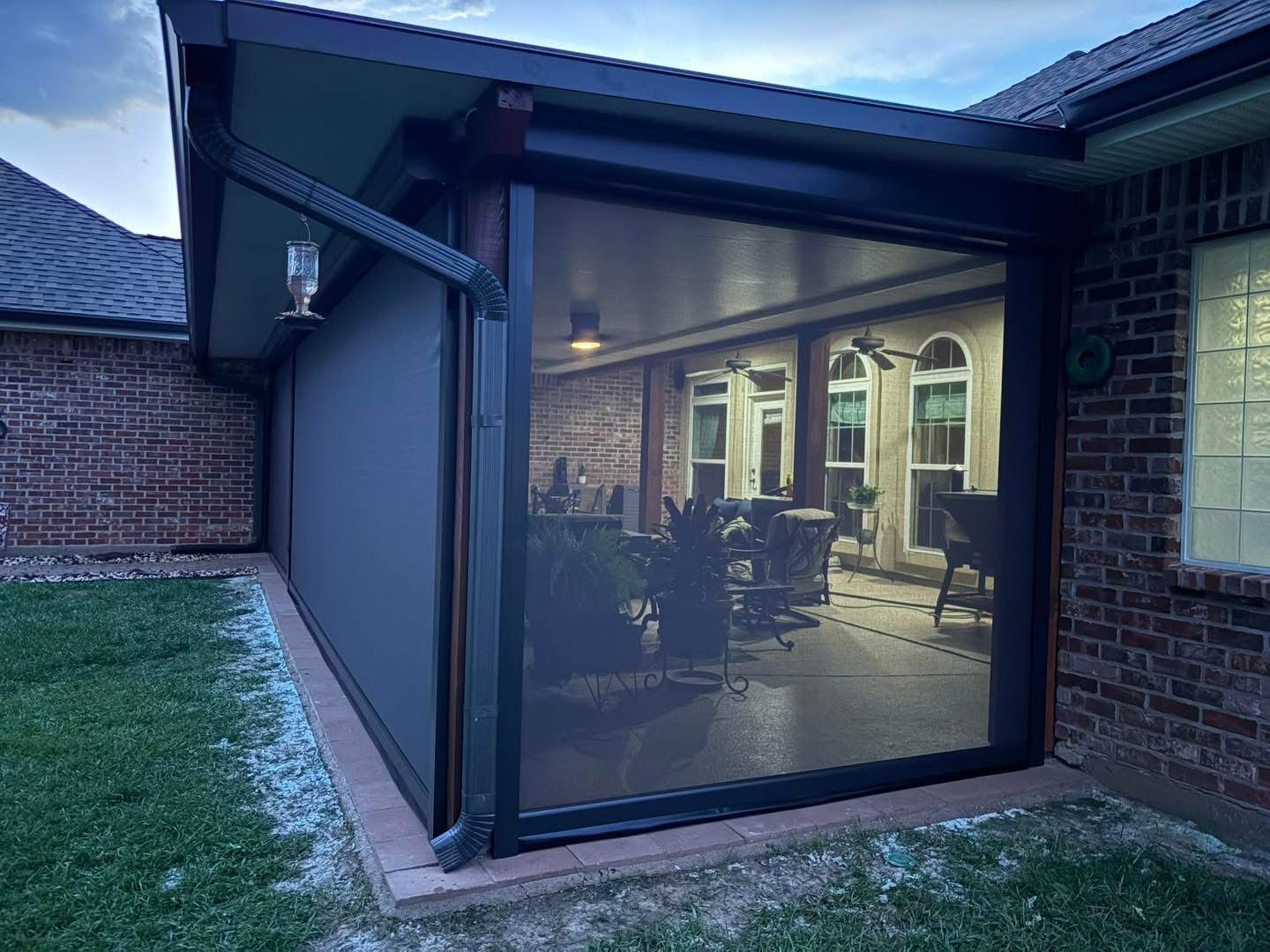 Black motorized shades lowered on a brick home patio at dusk